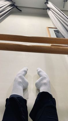 someone wearing white socks and black pants standing in front of a window