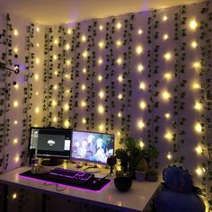 a computer desk topped with a desktop computer next to a wall covered in plants and lights