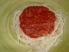 spaghetti and sauce in a green bowl on a yellow plate with a white napkin next to it