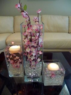 two glass vases with flowers and candles on a table in front of a couch