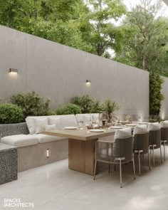 an outdoor dining area with white couches and wooden table surrounded by greenery on the wall