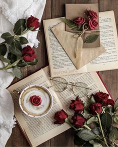 red roses are sitting on top of an open book next to two cups and saucers