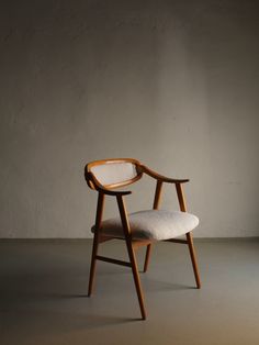 a wooden chair with a white cushion on the back and armrests, in front of a gray wall