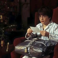 a young boy sitting in a chair holding a bag and paper while looking at something