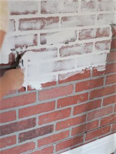 a person painting a brick wall with white paint