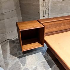 a wooden shelf sitting on top of a stone floor next to a bed with no sheets