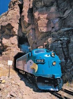 a blue train traveling through a rocky mountain side