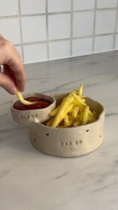 a person dipping french fries into a bowl with ketchup on the side,