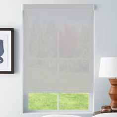 a bedroom with white walls and a window covered in roman shades, along with a bed