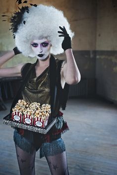 a woman with white hair and makeup is holding a tray of popcorn in her hands