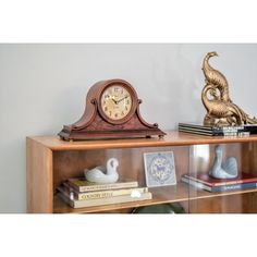 a wooden shelf with a clock, books and other decorative items on top of it