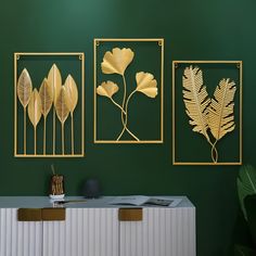 three gold metal wall art pieces on a green wall above a white cabinet with a black vase