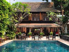 an outdoor swimming pool with tables and chairs around it, in front of a large house