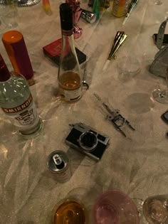 an assortment of alcohol and other items on a table with glasses, camera, bottle openers, etc