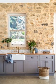 a kitchen with stone walls and gray cabinets, white counter tops and a window over the sink