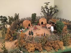 a miniature village with animals and people in the yard, surrounded by plants and trees