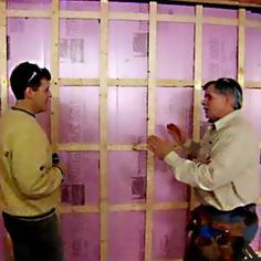 two men standing in front of a wall that is being framed with pink foam insulation