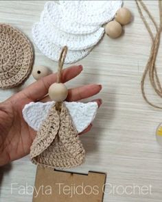 a hand holding a small crocheted angel ornament on top of a table