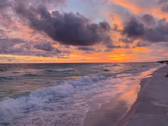 the sun is setting over the ocean with waves crashing on the shore and people walking along the beach