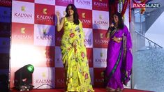 two women standing on stage with microphones in their hands and one woman wearing a yellow sari