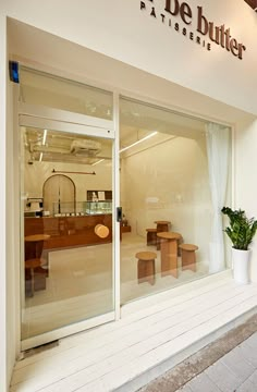 the outside of a store with glass doors and wooden benches in front of it, along with a potted plant