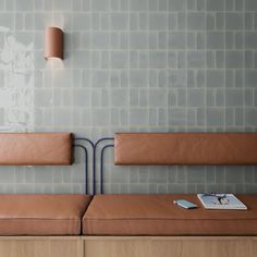 two brown benches sitting next to each other in front of a wall with tiles on it