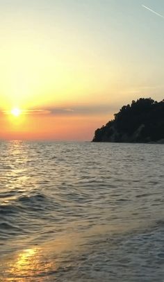 the sun is setting over an island in the middle of the ocean with small waves