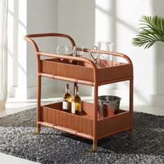 a wooden bar cart with wine glasses and bottles on the bottom shelf next to a potted plant