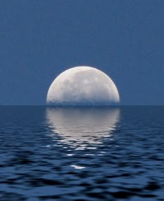 the full moon is reflected in the water on a clear day with dark blue skies