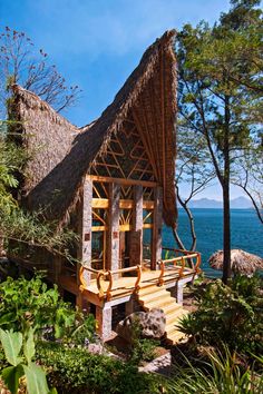 a wooden structure with thatched roof next to the ocean and trees in front of it