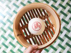 a person holding up a small white ball in a bamboo holder on a green and white checkered wall