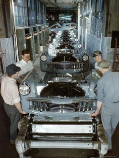 three men working on an old car in a garage with another man looking at it