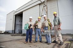 four men standing in front of a building with hard hats and safety equipment on their shoulders