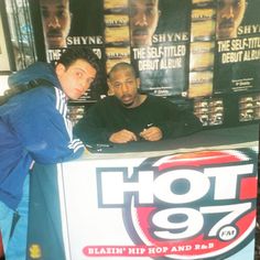 two men standing in front of a counter with a sign that says hot 97 on it