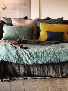 a bed with lots of pillows and blankets on it in a room that has wooden floors