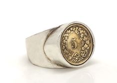 a silver and gold signet ring with a coin on the center, in front of a white background