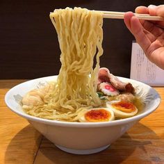 someone is holding chopsticks above a bowl of ramen with eggs and meat