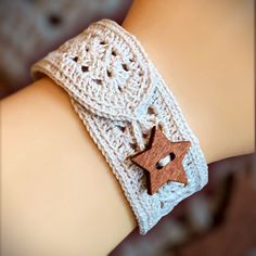 a close up of a person's arm wearing a crocheted bracelet with two wooden stars on it