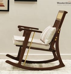 a wooden rocking chair with white cushions and gold trim on the armrests, in front of a wall