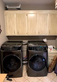 two washers and dryer in a small room with cabinets on the wall behind them