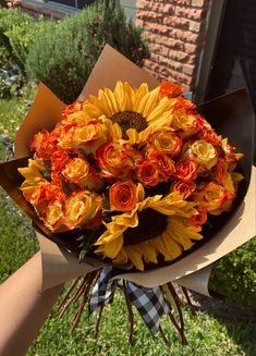 a bouquet of sunflowers and roses is held by someone's hand in front of a house