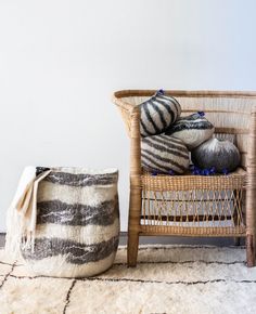 a wicker chair sitting next to a basket filled with pillows on top of a rug