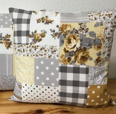 two pillows sitting on top of a wooden table next to each other, one is made out of patchwork and the other has flowers