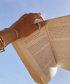 a person is holding an open book in their left hand and wearing gold bracelets