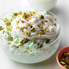 a bowl filled with whipped cream and pistachio toppings next to a bowl of nuts