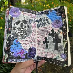 someone is holding up an altered book with skulls and flowers on it in front of some bushes