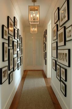 a long hallway with pictures on the wall and framed photos on the walls, along with a light fixture