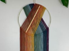 a multicolored wall hanging on a white wall next to a potted plant