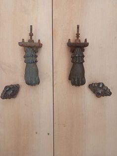 three cast iron hand and foot hooks hang on wood paneled doors, with one holding a cat's paw