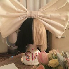 a wig with a bow on top of it and flowers in front of the hair